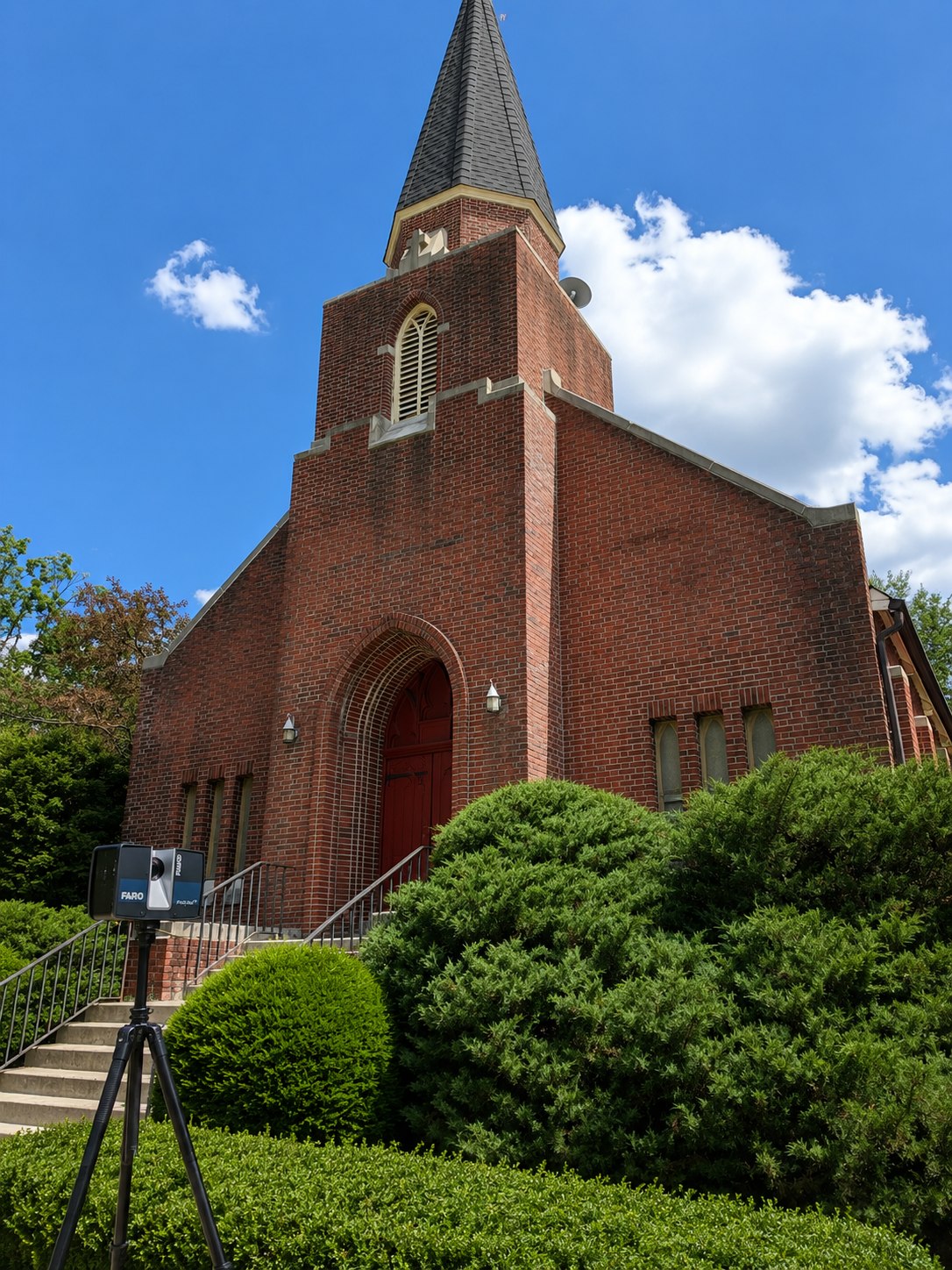 FARO laser scanner on a tripod in front of a historic brick church in Danbury, CT, with a tall steeple and arched red entrance door